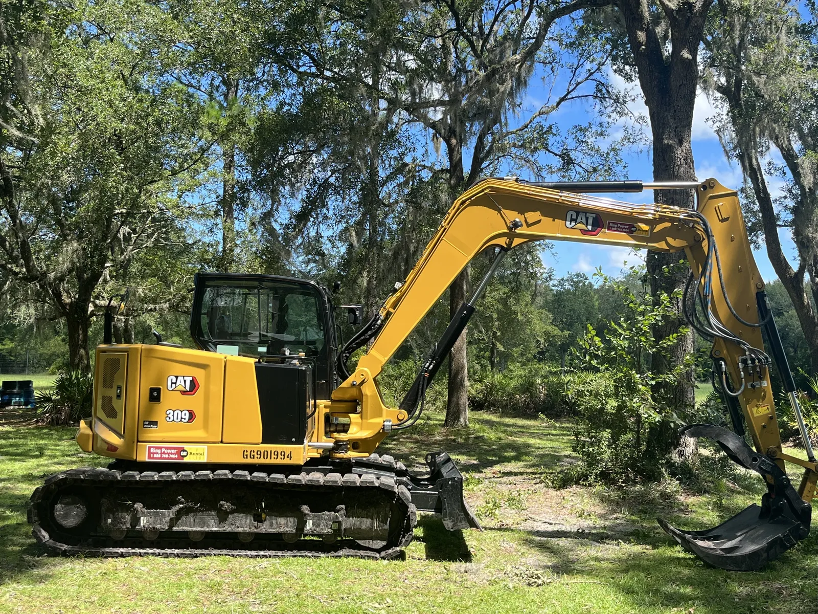 Our compact excavator with bucket and thumb on the boom, under live oaks and Spanish moss