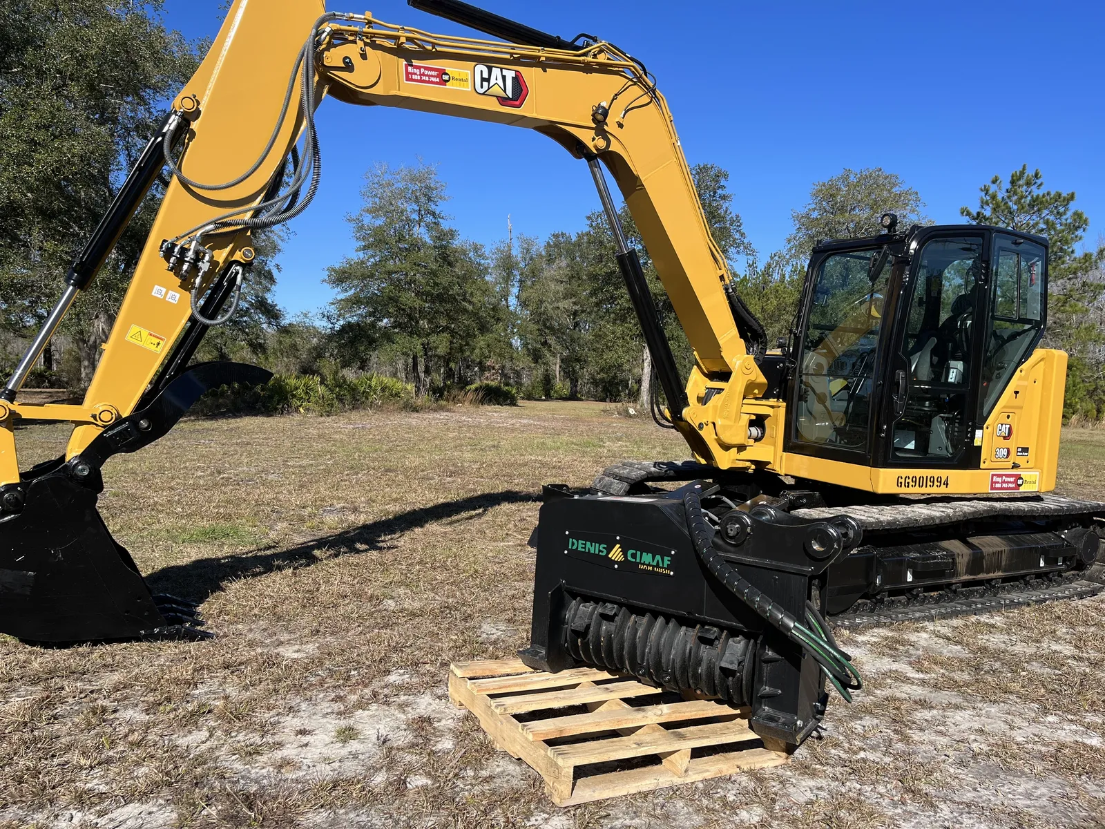 Our excavator parked in an open field beside its drum mulching head resting on a pallet, near Monticello, FL